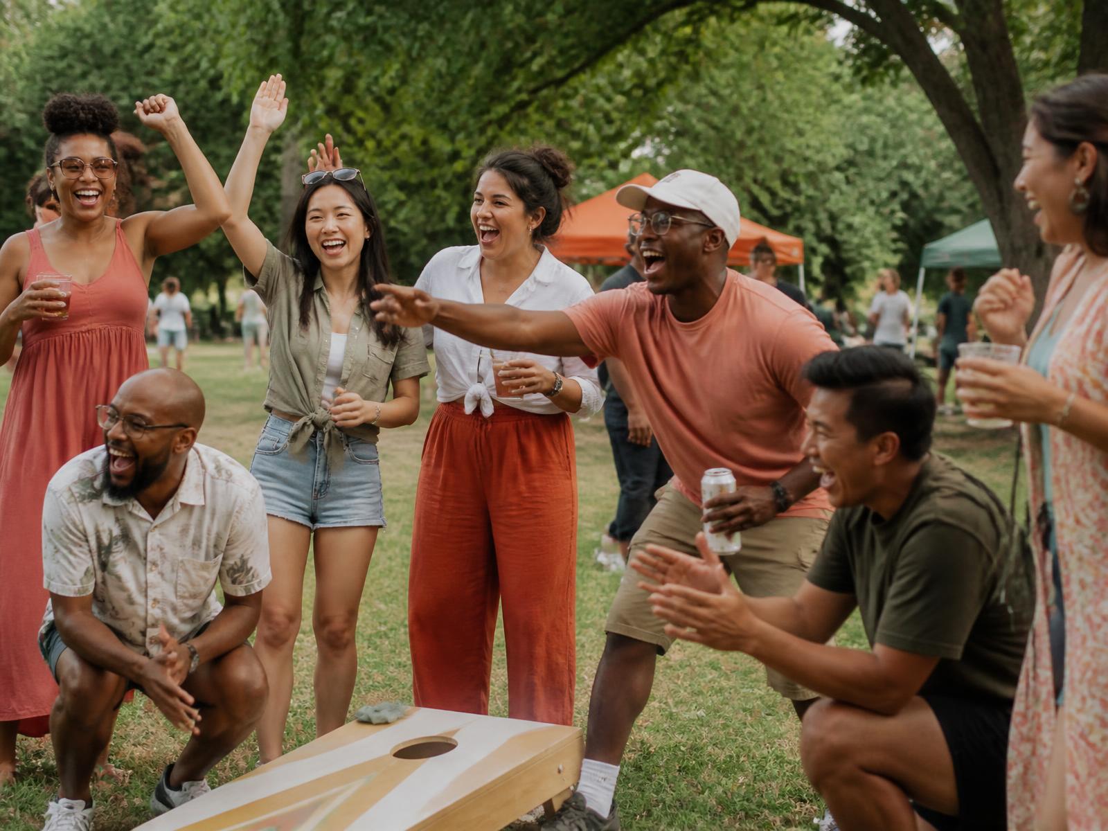 Friendsival guests cheering during a lawn game at a summer social in the park
